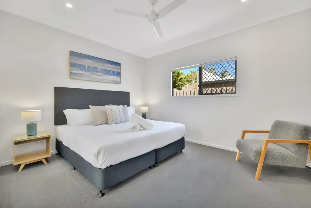 Bedroom with a large bed, grey armchair, bedside lamp and seascape artwork