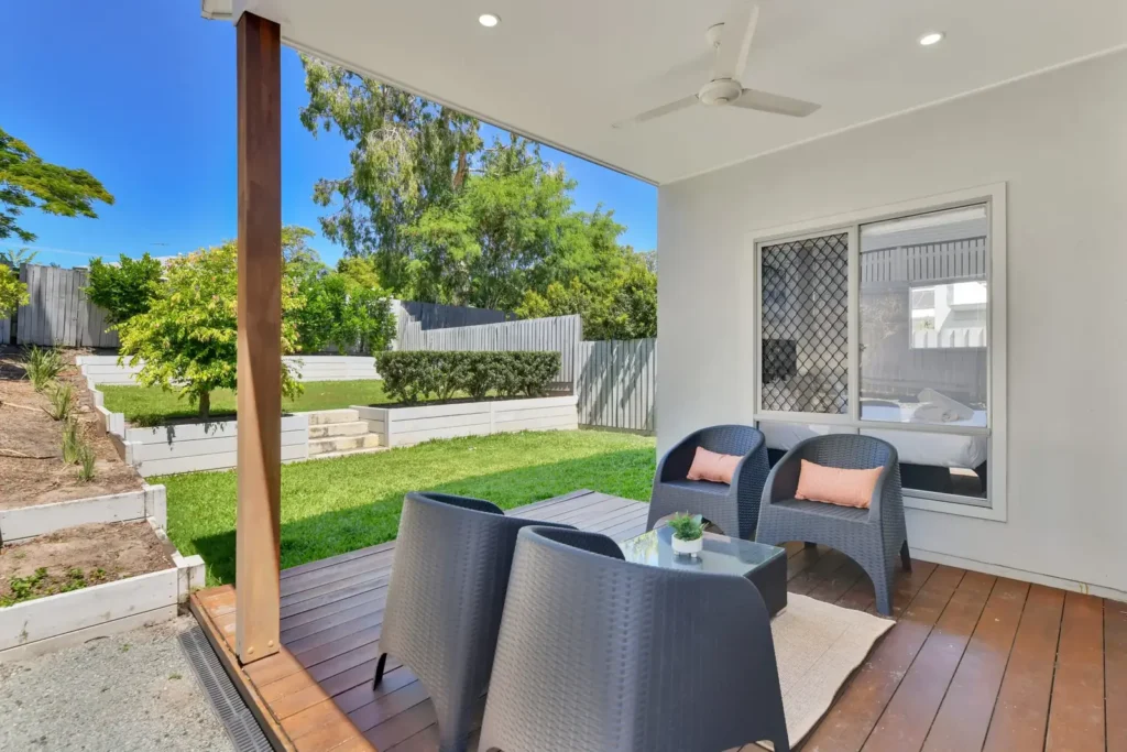 Covered back deck with outdoor lounge chairs and a ceiling fan, looking over the lawn