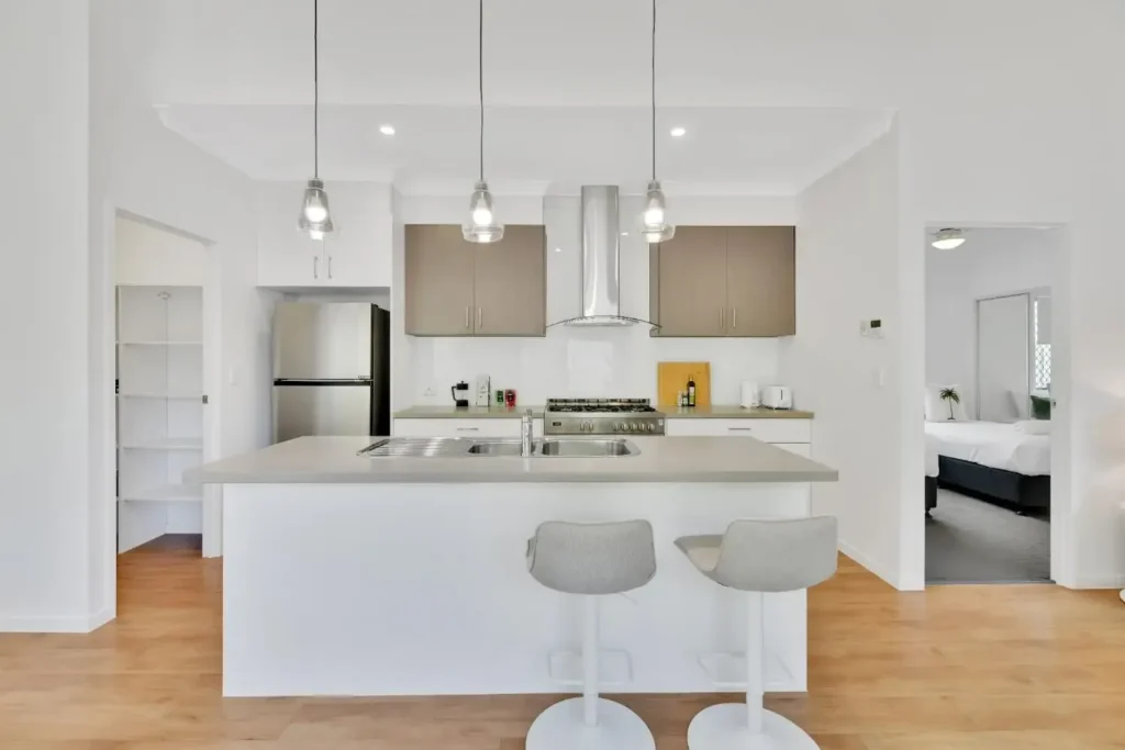 Kitchen with stone island bench, bar stools, gas cooktop, rangehood and pantry shelving