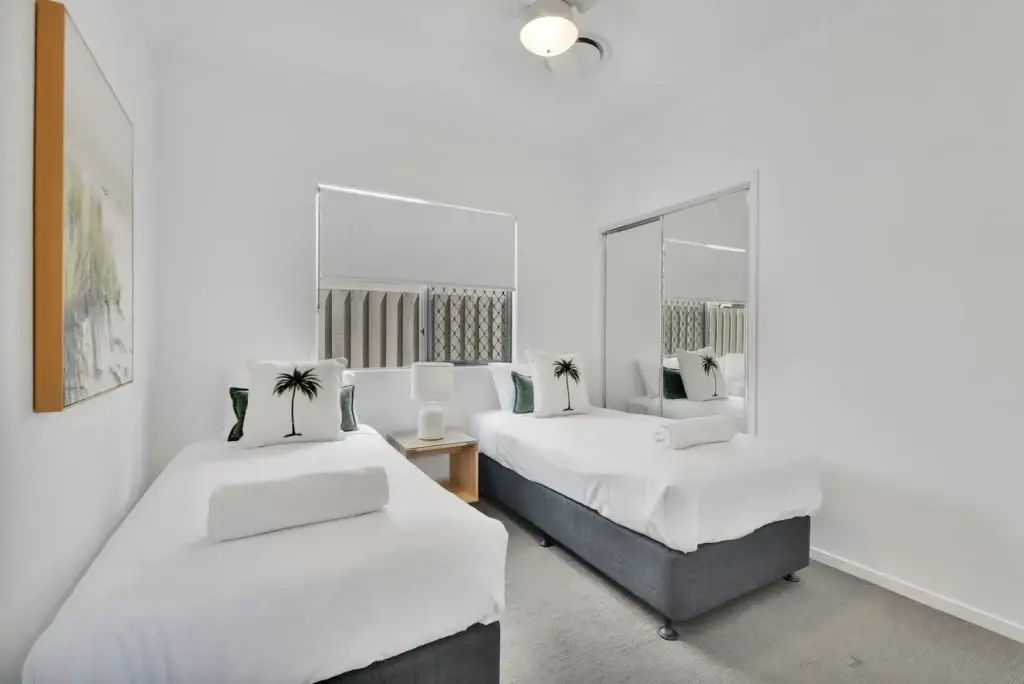 Twin bedroom with two single beds, palm-print cushions and a mirrored built-in wardrobe